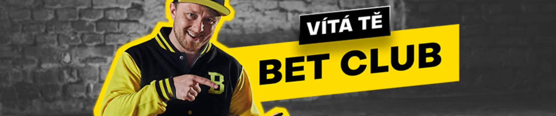 Vítej v BET CLUBU – žluto-černý banner. Muž v žluto-černé bundě s písmenem „B“ a kšiltovkou ukazuje na žlutý banner s nápisem „Vítá tě BET CLUB“ na cihlovém pozadí.